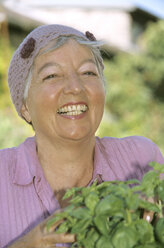 Lächelnde ältere Frau mit Basilikumpflanzen in der Hand, Nahaufnahme - PEF00325