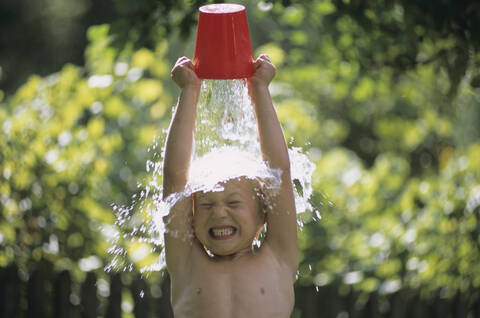 Junge, der sich Wasser über den Kopf gießt, im Freien, lizenzfreies Stockfoto