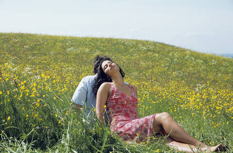 Young couple sitting back to back in meadow stock photo