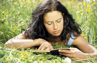 Young woman lying on grass reading book - LDF00086