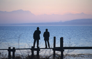 Silhouette of man and women standing on boardwalk, rear view, Ammersee, Bavaria, Germany - UMF00111