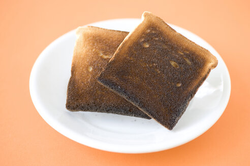 Zwei Scheiben verbranntes Toastbrot auf einem Teller, Nahaufnahme, Blick von oben - MNF00093
