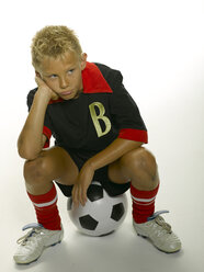 Boy (8-11) sitting on soccer ball, looking to side - LMF00131