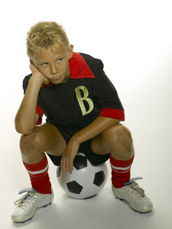 Junge (8-11) sitzt auf einem Fußball und schaut zur Seite - LMF00131