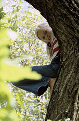 Girl (8-9) lying on tree branch, low angle view - CRF00602