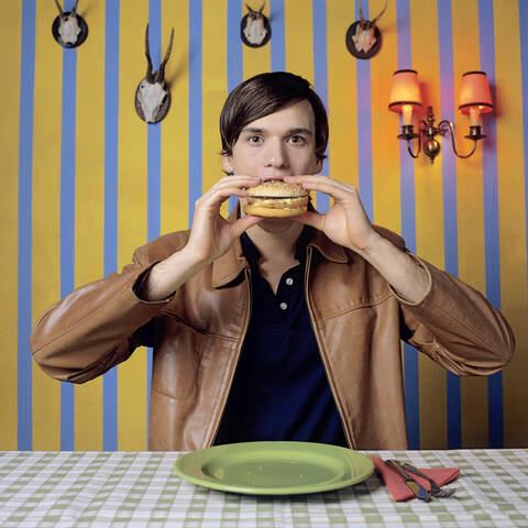 Junger Mann isst Burger, Porträt, lizenzfreies Stockfoto