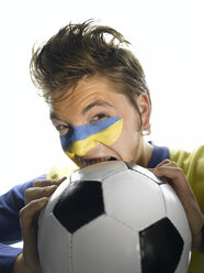 Junger Mann mit ukrainischer Flagge im Gesicht, beißt in einen Fußball, Nahaufnahme - LMF00359