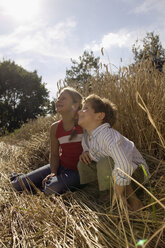 Boy and girl (6-9) sitting in wheat field, looking up - CKF00114