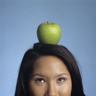 Young woman balancing apple on head, looking up, close-up - JLF00025