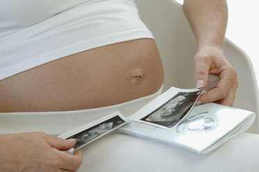 Pregnant woman looking at ultrasound images of baby, close-up - CRF00724
