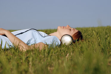 Woman lying in grass listening to music - CLF00044