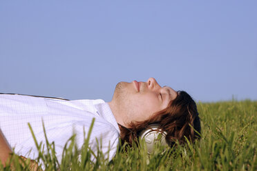 Man lying in grass listening to music - CLF00043