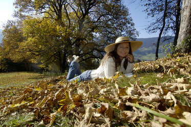 Young woman lying on autumn leaves with hand on chin, portrait - HHF00141