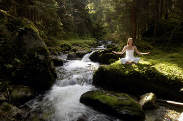 Woman meditating in forest by stream - HHF00136