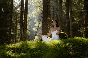 Junge Frau meditiert im Wald und schaut weg - HHF00132