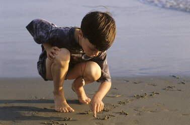 Junge (6-7) schreibt auf Sand am Strand - CRF00734