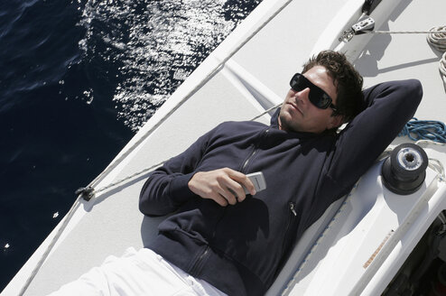 Mann auf Segelboot liegend mit Mobiltelefon - RDF00090