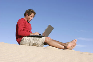 Mann sitzt mit Laptop auf Sand in der Wüste - RDF00058