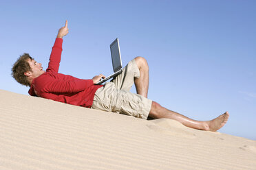 Mann auf Düne liegend mit Laptop - RDF00055