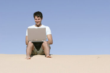 Mann sitzend auf einer Düne mit Laptop - RDF00040