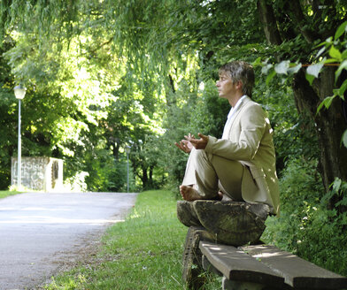 Man sitting on park bench, meditating - DKF00098