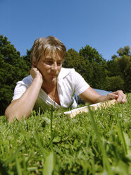 Man reading book lying on grass - DKF00096