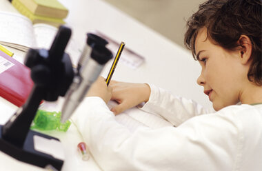 Boy (8-9) sitting by microscope, writing - WESTF00073