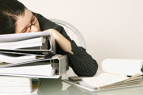 Mid adult woman sleeping at work resting head on pile of files - 00039LRH-U