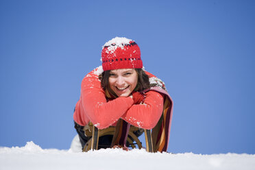 Frau mit Schnee bedeckt auf Schlitten liegend, lächelnd - WESTF00174