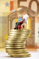 Figur im Rollstuhl und Betreuerin auf einem Haufen Münzen - 03138CS-U