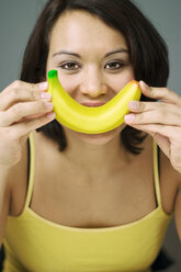 Young woman holding banana to mouth, close-up, portrait - MFF00157