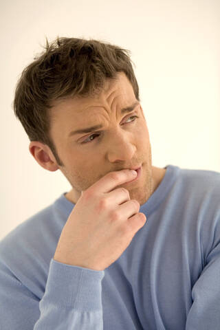 Young man with finger on lips, looking away, close-up stock photo