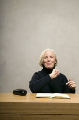 Ältere Frau sitzt mit Buch am Tisch, lächelnd - WESTF00671