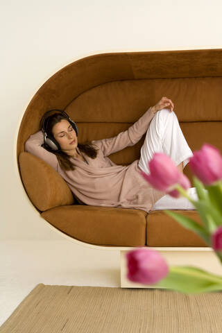 Frau entspannt auf Sofa mit Kopfhörern, rosa Tulpen im Vordergrund, lizenzfreies Stockfoto