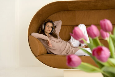 Junge Frau auf dem Sofa liegend, mit Kopfhörern - WESTF00546