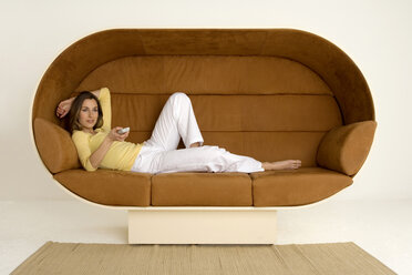 Young woman lying on sofa holding remote control, smiling - WESTF00534