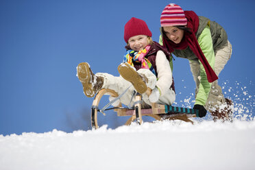 Austria, teenage girl (16-17) pushing girl (6-7) on sledge, smiling, low angle view - WESTF00719
