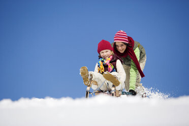 Austria, Teenage girl (16-17) pushing girl (6-7) on sledge, smiling, low angle view - WESTF00718