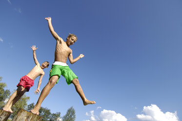 Austria, boys (10-11) jumping from logs into water, low angle view - HHF00393