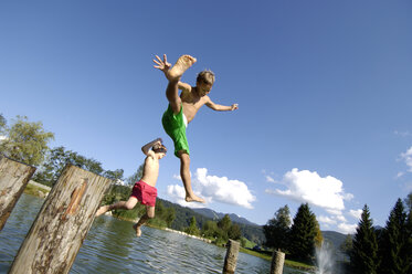 Austria, boys (10-11) jumping from logs into water, low angle view - HHF00392