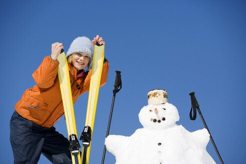 Österreich, Mädchen (12-13) mit Skiern neben Schneemann stehend, lächelnd, Porträt - WESTF00729