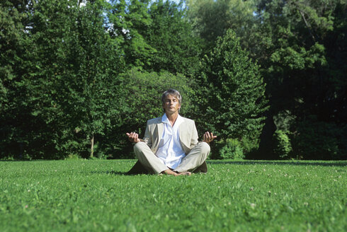 Mid adult man meditating in park, ground view - DKF00106