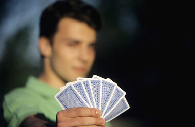 Junger Mann hält Spielkarten, Fokus auf Karten im Vordergrund, Nahaufnahme - WESTF01191
