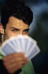 Young man holding playing cards, focus on man at background, close-up - WESTF01189