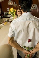 Mann sieht Frau an, die Rose hinter dem Rücken hält - CLF00192
