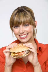 Junge Frau mit Hamburger in der Hand, lächelnd, Porträt, Nahaufnahme - WESTF01317