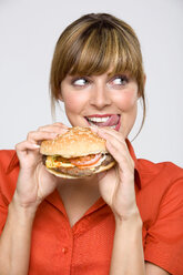Young woman holding hamburger, licking lips, close-up - WESTF01316