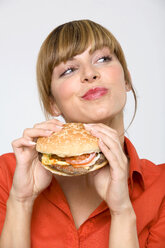 Young woman holding hamburger, sideways glance, close-up - WESTF01313