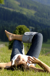 Woman lying in field using mobile phone - WESTF01458
