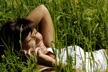 Frau liegt auf einem Feld und benutzt ein Mobiltelefon, lächelnd, Blick von oben - WESTF01447